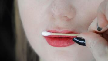 Beautician examines lips with cotton swab after permanent makeup, close-up view showing red-tinted lips and detailed skin texture during a post-procedure check video