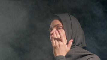 woman wearing hijab appears contemplative while surrounded fog showcasing her emotions in creative indoor performance setting dusk, applies cream to face video