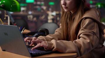 Female student listening to favorite songs and solving a school assignment, working on her laptop under a green lamp in a quiet university library. Higher education diploma. Camera A. video