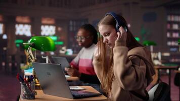 Young student attending to a web lecture with headset in the campus library, takes notes and learns about politics in an online meeting. Focused pupil during class lesson. Camera A. video