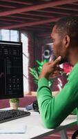 Vertical African american man using PC to purchase and sell stocks, monitoring forex graphs and diagrams. Male broker looking at stock exchange candle stick charts on computer. Camera B. video