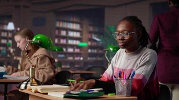 University student engrossed in texting with classmates at the library, chatting with friends instead of studying. Girl discussing with colleagues about an assignment. Camera A. video