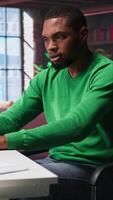 Vertical Black man doing remote work feeling uneasy and anxious at desk, shaking his legs and being jittery due to task completion and deadline. Freelancer working under pressure, anxiety. Camera B. video