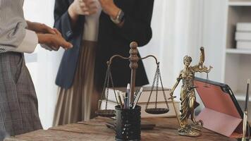 Two business people standing in front of a desk with a statue of justice video