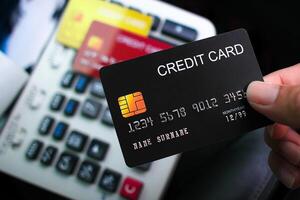 A hand holds a black credit card over a card reader or keypad, suggesting a transaction or payment process. Electronic payment, credit card processing. photo