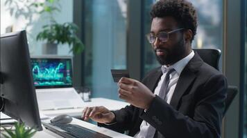 Happy joyful African American man holding banking credit card online buying consumer payment computer buyer businessman male guy shopper business manager employee entrepreneur office client purchase video