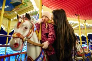 Joyful mother and daughter share a moment on a carousel at night photo