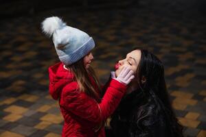 Mother and daughter share a playful moment outdoors at night during winter, capturing joy and warmth photo