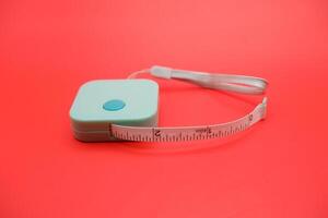 Green metric measuring tape coiled and isolated on vivid red background. Perfect for concepts related to tailoring, diet, or fitness. photo