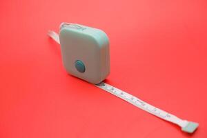 Flexible green measuring tape rolled neatly against a red background. Clean studio shot with strong contrasting colors. photo