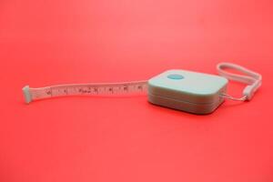 Minimal photo of green measuring tape on a plain red backdrop. Flat lay composition suitable for banners, posters, or editorial design.