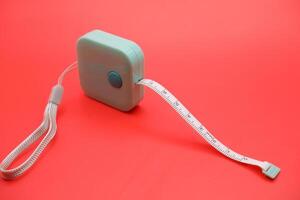 Green measuring tape isolated on red background. Flexible tailor tape for body measurements, presented in a bold color contrast. photo
