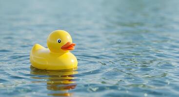 Yellow rubber duck floating peacefully on rippling blue water surface, evoking innocence photo