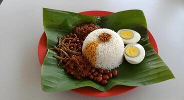 Authentic nasi lemak dish with rice, sambal, eggs and peanuts on banana leaf photo