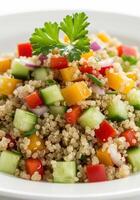 A vibrant and nutritious quinoa salad is presented with fresh vegetables on a white plate. photo