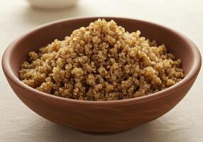 A brown bowl of cooked quinoa sits invitingly on a textured, neutral colored surface. photo