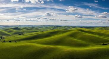An expansive view of lush green rolling hills under a bright, partly cloudy sky. photo