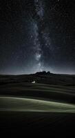 The Milky Way arches over the rolling hills, creating a breathtaking view at night. photo