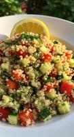 A refreshing quinoa salad with vibrant tomatoes, cucumbers, and a lemon slice garnish. photo