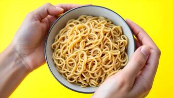 Hands Holding Bowl of Noodles on Bright Yellow Background Ready to Eat photo