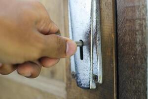 Opening an old wooden door with a key. Close up of a person's hand inserting a key into the keyhole of an old, worn-out wooden door to open it photo