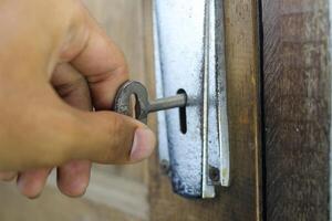 Opening an old wooden door with a key. Close up of a person's hand inserting a key into the keyhole of an old, worn-out wooden door to open it. photo