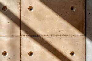 Sunlight creating shadows on textured concrete wall with holes photo