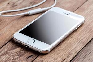 White smartphone lying on wooden table with earphones plugged in photo