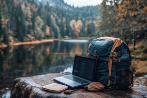 Laptop and backpack resting on log overlooking serene lake in autumn forest photo