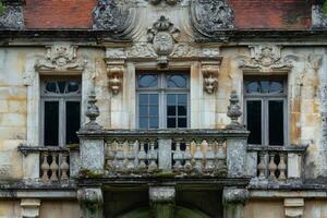 Elegant balcony and windows of an ancient french chateau showing stone ornaments and red tile roof photo
