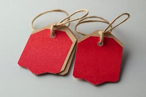 Two red blank cardboard tags with string on gray background photo