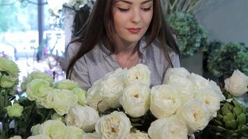 Charming female florist admires delicate white roses in a vibrant flower shop video