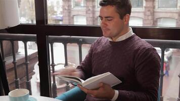 Man enjoys reading a book while sipping coffee at a cozy cafe video