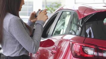 Joyful woman capturing memories with her smartphone beside her new car video