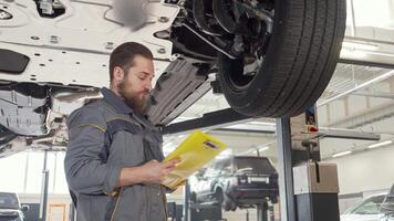 Focused mechanic inspecting lifted vehicle while taking notes video