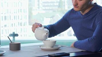 Cheerful man pouring tea while engaging with his smartphone video