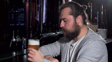 Bearded man in a gray sweater sipping beer, lost in thought at the bar video