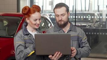 Bearded car mechanic collaborates with red-haired female technician using laptop video