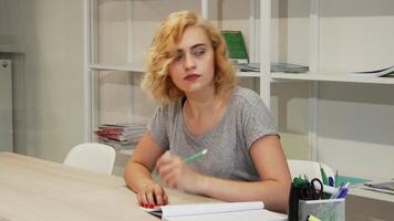 Thoughtful young woman jotting down notes while studying video