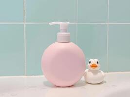 A bottle of pink liquid soap sits on a counter next to a rubber duck photo