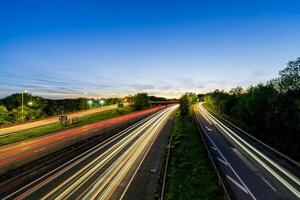 Light trails illuminating highway at dusk, creating dynamic streaks across asphalt under twilight sky photo