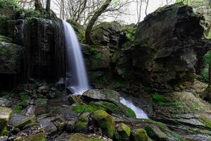 Waterfall cascading down mossy rocks in lush green forest photo