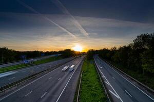 Cars driving fast on highway at sunset with contrails in the sky photo