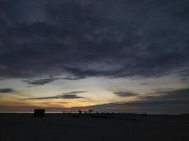 Serene beach sunset. Dark silhouettes against a vibrant, colorful sky. Perfect for travel, nature, or tranquility themes. Evokes peace and the end of day. photo