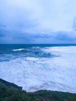 Dramatic seascape featuring turbulent waves crashing against a rugged coastline under an overcast sky. Powerful natural scenery. Ideal for themes of resilience or raw beauty. photo