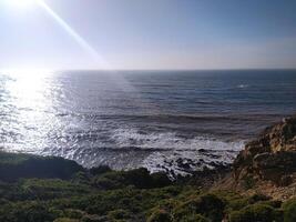 Coastal cliff view roug waves crashing against the rocks in the afternoon sunlight at a scenic seaside location photo