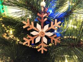 Rustic wooden snowflake ornament hanging on a Christmas tree, illuminated by warm and cool lights. Perfect for holiday cards, websites, and festive designs. photo