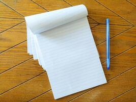 Blank lined notepad and blue pen on a wood table. Perfect for education, business, or office concepts. Clean, simple, and ready for your message. Ideal for mockups or website backgrounds. photo