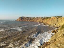 Coastal cliff view of rough waves crashing against the rocks afternoon sunlight at a scenic seaside location photo