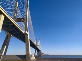 Stunning lowangle view of a modern cablestayed bridge stretching across a calm body of water under a vibrant blue sky. Ideal for architecture, travel, engineering, and infrastructure projects. photo